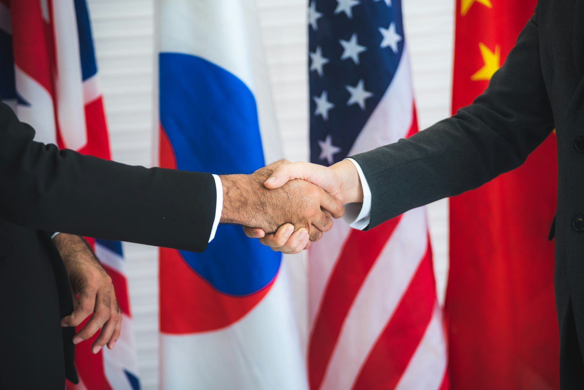 Business people shake hands, international flag background