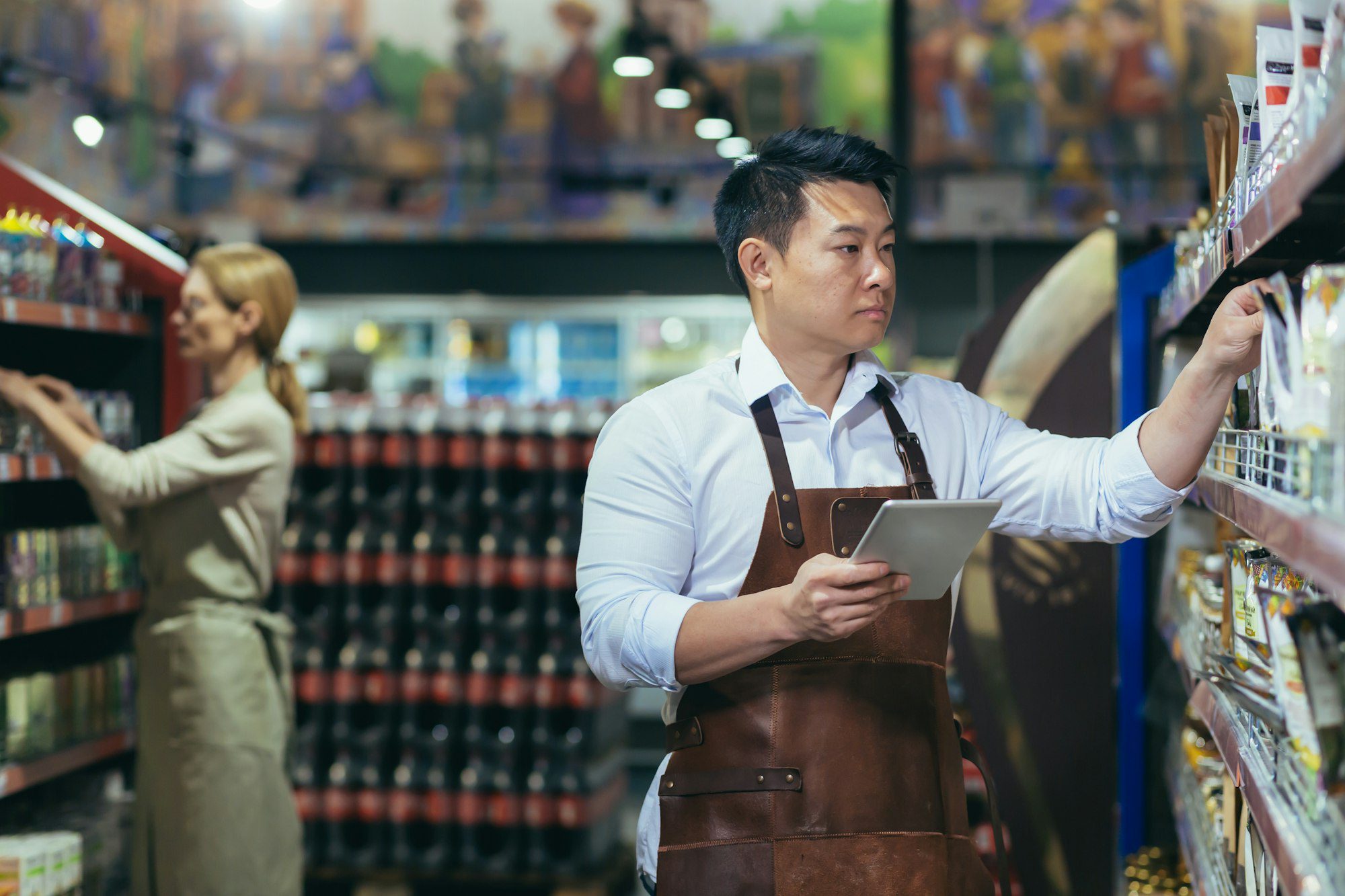 two workers in a supermarket in the grocery department arrange products an asian man with tablet